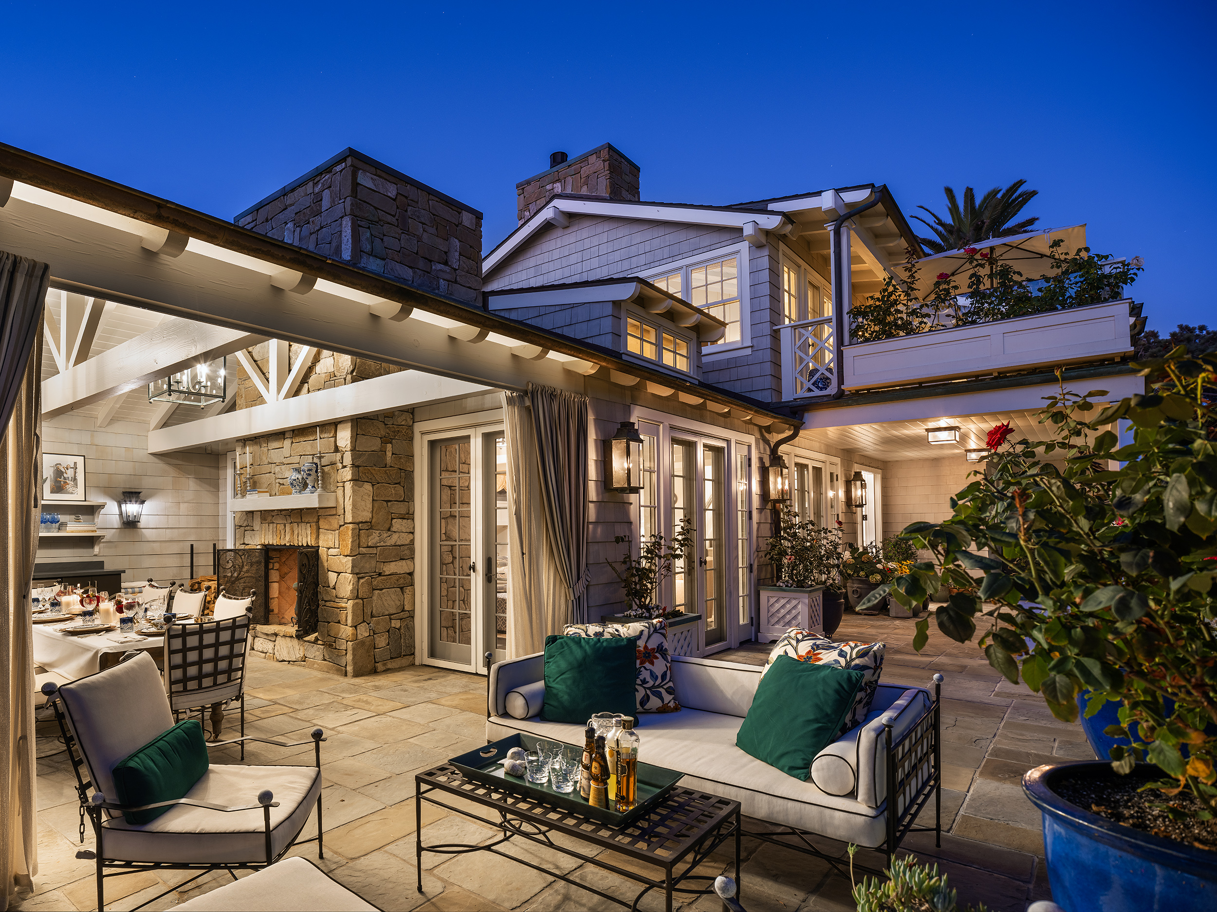 Elegant outdoor patio and seating area at night, with cozy lighting, plants, and a view of a modern house.